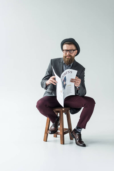 Businessman with vintage mustache and beard reading business newspaper while sitting on stool