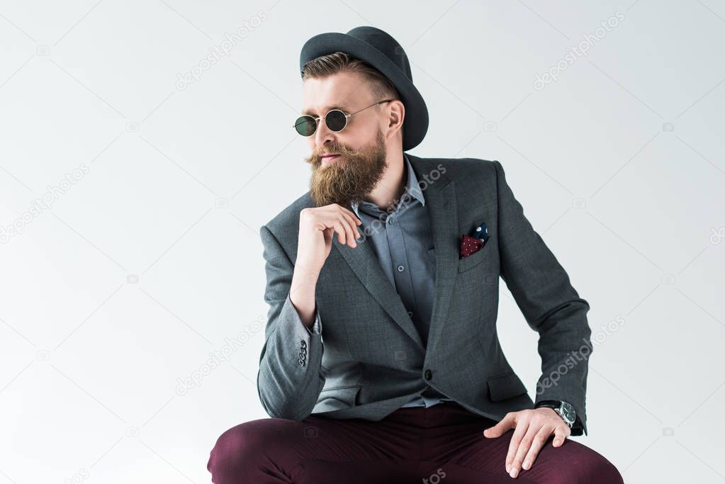 Handsome man in vintage style clothes wearing hat and sunglasses isolated on light background