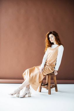 Ahşap taburede oturan uzun kızıl saçlı kadın