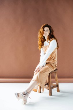 Gülümseyen ve ahşap taburede oturan güzel genç kız