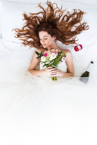 Top view of redhead bride wearing white dress sleeping in bed with flowers and wedding rings