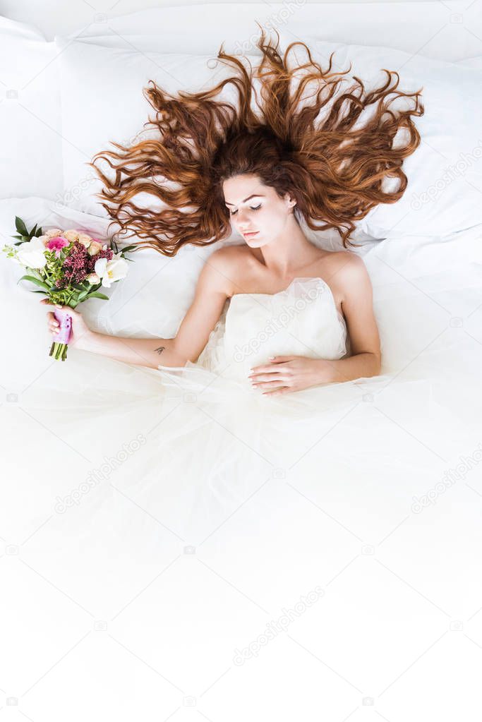 Top view of bride wearing white dress sleeping in bed with flowers bouquet