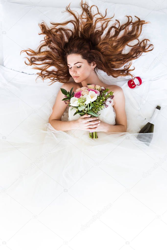 Top view of redhead bride wearing white dress sleeping in bed with flowers and wedding rings