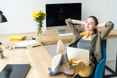 elleri başının arkasında oturan ve uzak ofis seyir dizüstü bilgisayar ile şık iş kadını
