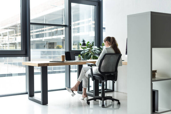 back view of businesswoman sitting at workplace in modern office