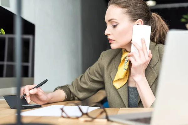 Mulher Negócios Concentrada Usando Calculadora Falando Por Smartphone Escritório — Fotografia de Stock