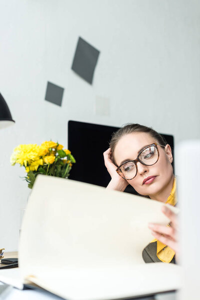 close-up view of bored businesswoman in eyeglasses working with papers at workplace