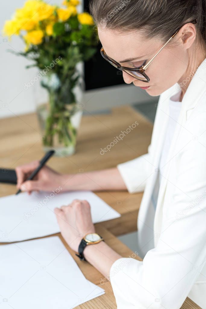 selective focus of businesswoman checking time while doing paperwork at workplace in office