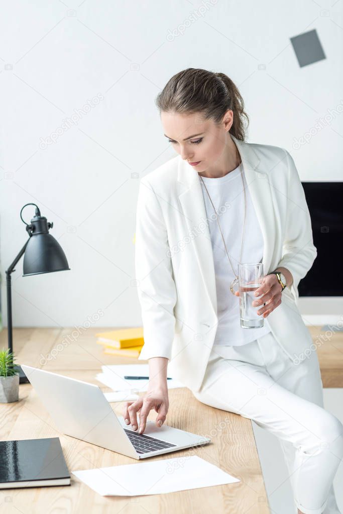 businesswoman with glass of water working on laptop at workplace in office