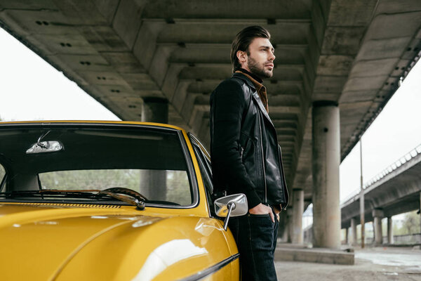 side view of stylish man standing near yellow retro car and looking away