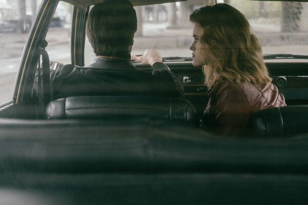 Вид сзади стильной девушки, смотрящей на красивого бойфренда за рулем автомобиля
