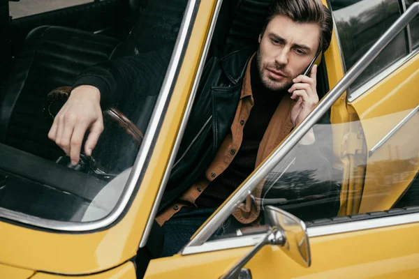 黄色のクラシックカーに座りながらスマート フォンで語っているハンサムなスタイリッシュな男 — ストック写真