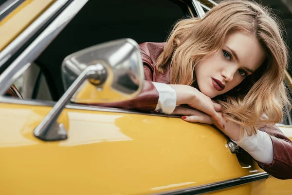 美丽的时尚女孩看着相机通过车窗的复古车 — 图库照片