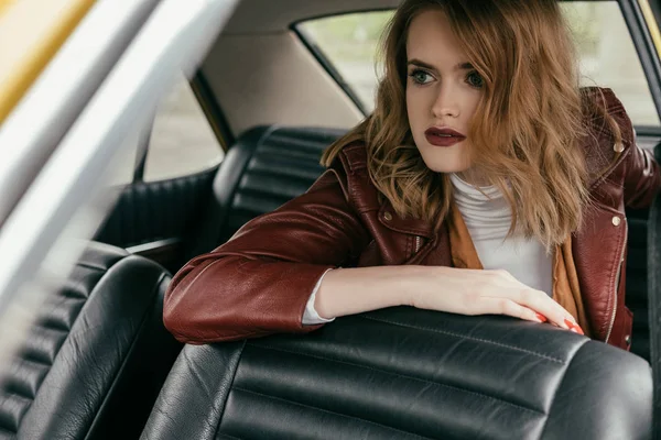 漂亮的年轻女子穿着皮夹克坐在经典的车 看着远离 — 图库照片