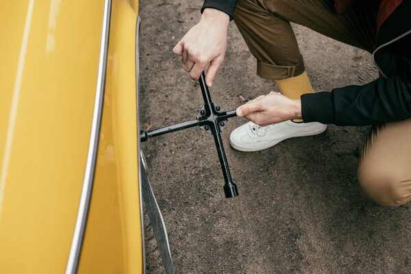 cropped shot of man in leather jacket fixing wheel of yellow vintage car 