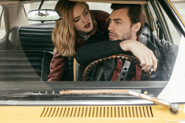 соблазнительная девушка смотрит на красивого парня за рулем старомодного автомобиля
 