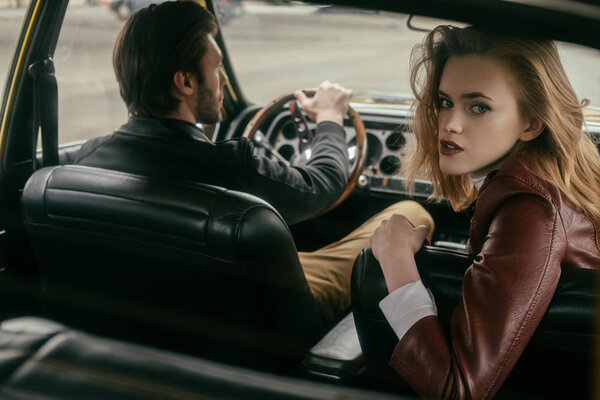 стильная девушка смотрит в камеру, сидя в машине с красивым бойфрендом
