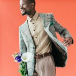 Stylish african american man in vintage jacket with flowers, on red
