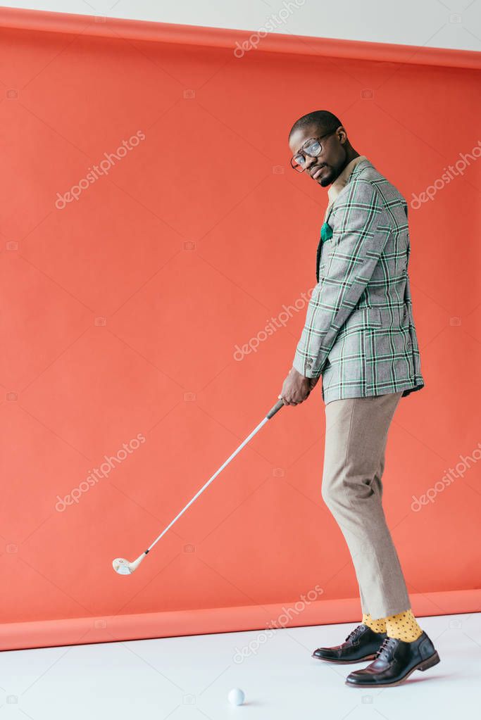 Fashionable african american man playing golf, on red