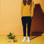 Homme à la mode avec les cheveux longs debout près de la plante, sur jaune