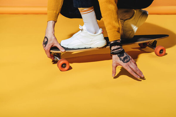 низкий вид скейтбордиста в белых кроссовках на длинной доске, на желтом

