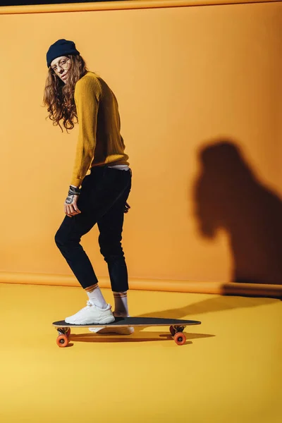 handsome stylish man standing on skateboard, on yellow