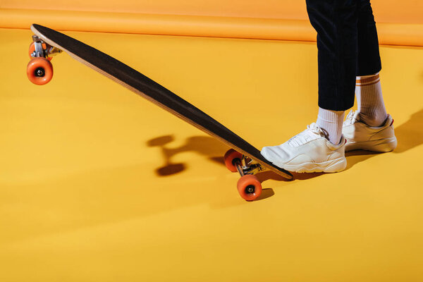 cropped view of stylish man in white sneakers with longboard, on yellow