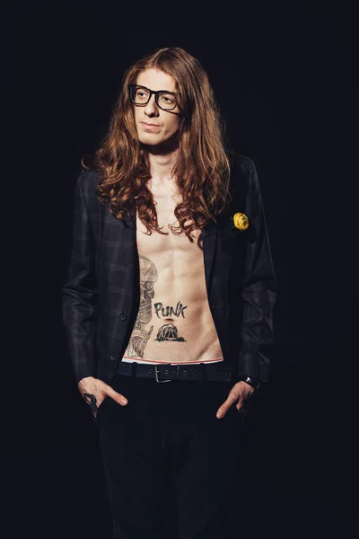 shirtless tattooed man with long hair posing for fashion shoot, isolated on black