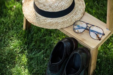 Yeşil çimenlerin üzerinde ahşap merdiven üzerinde gözlük, siyah ayakkabı ve şapka düzenlemenin görünümü kadar kapatın