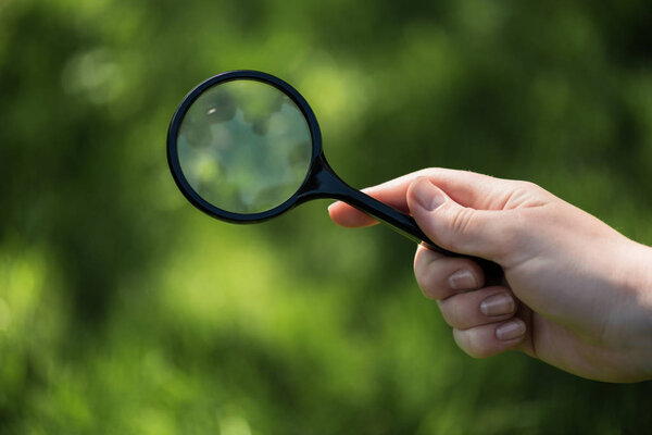 partial view of woman with magnifying glass in hand on green blurred backdrop