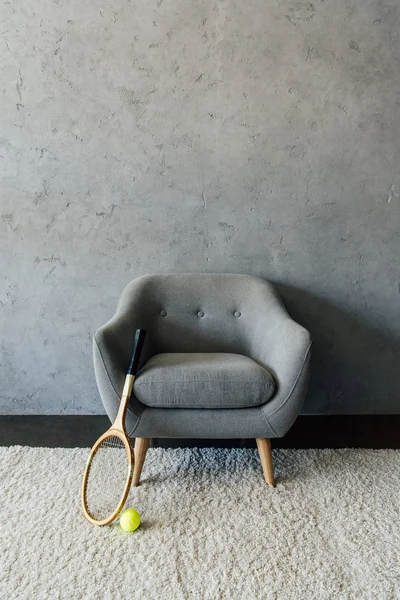 Tennis racket and ball with grey armchair — Stock Photo