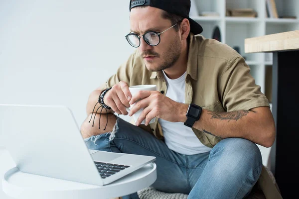 Homme avec tasse de café regardant ordinateur portable — Photo de stock