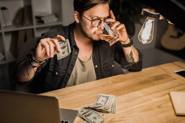 Man drinking whiskey with pile of cash — Stock Photo