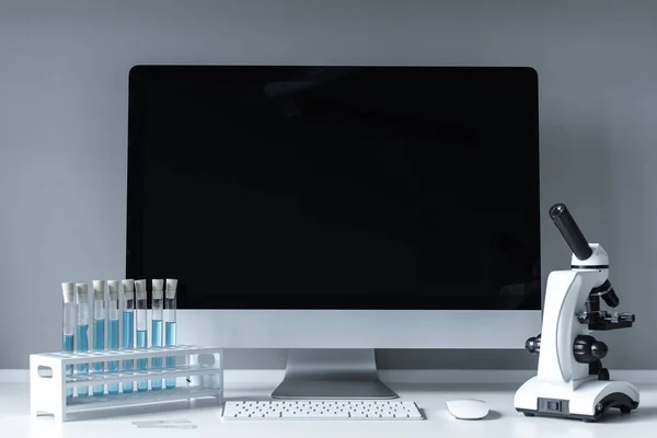 Microscope and test tubes with liquid on working table near computer — Stock Photo