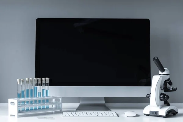 Microscopio y tubos de ensayo con líquido en la mesa de trabajo cerca de la computadora - foto de stock