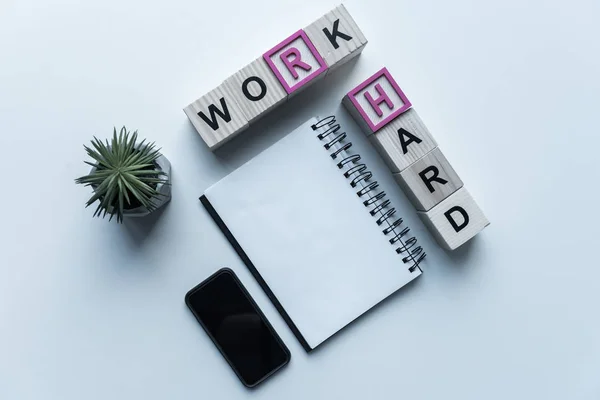 Vista superior de cubos de madera con palabras Trabajar duro y portátil en la mesa - foto de stock