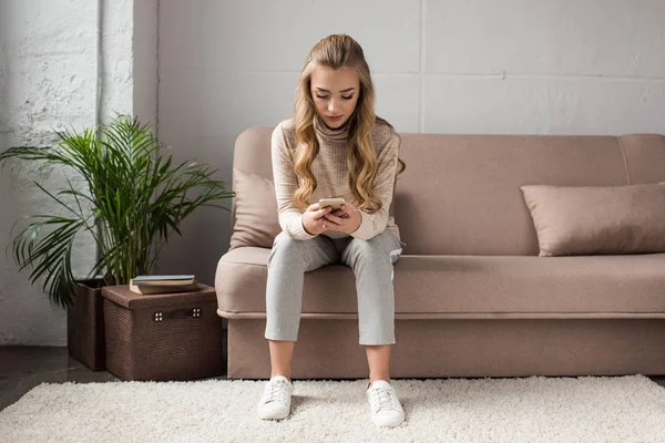 Jeune femme utilisant un smartphone tout en étant assis sur le canapé dans le salon élégant — Photo de stock