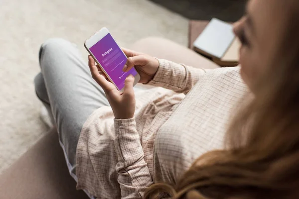 Recortado tiro de la mujer en el sofá con el teléfono inteligente con aplicación instagram en la pantalla - foto de stock