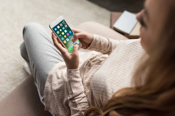 Recortado tiro de la mujer en el sofá con el teléfono inteligente con aplicaciones iOS en la pantalla - foto de stock