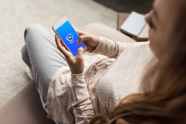 Tiro recortado de mulher no sofá usando smartphone com aplicativo shazam na tela — Fotografia de Stock