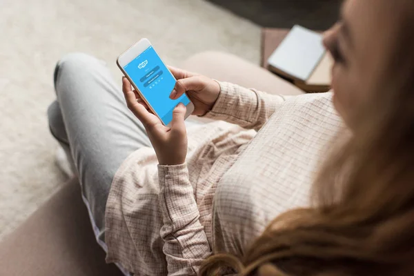 Recortado tiro de la mujer en el sofá con el teléfono inteligente con la aplicación de Skype en la pantalla - foto de stock