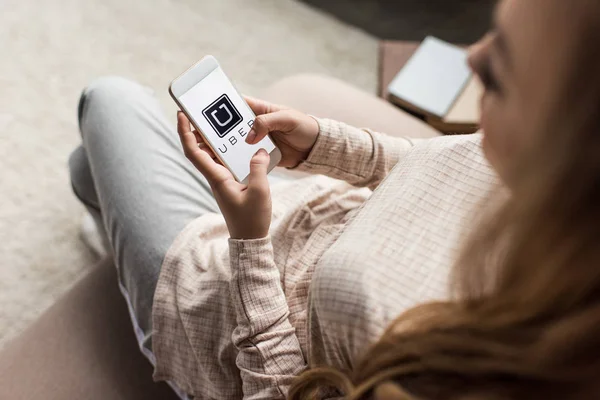 Recortado tiro de la mujer en el sofá con el teléfono inteligente con el logotipo uber en la pantalla - foto de stock