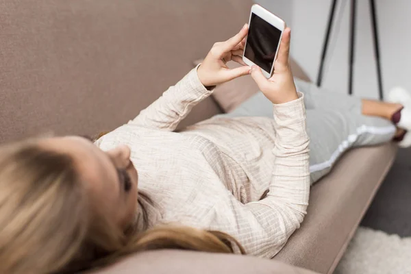 Jovem mulher usando smartphone enquanto relaxa no sofá em casa — Fotografia de Stock