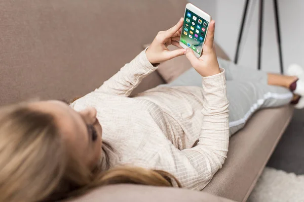 Woman on couch using smartphone with ios apps on screen — Stock Photo