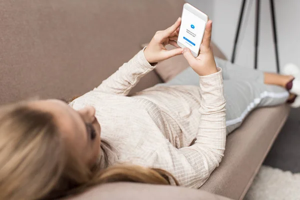 Mujer en el sofá utilizando el teléfono inteligente con aplicación de mensajero en la pantalla - foto de stock