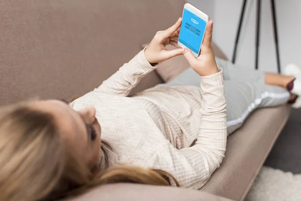 Mujer en el sofá utilizando el teléfono inteligente con la aplicación de Skype en la pantalla - foto de stock