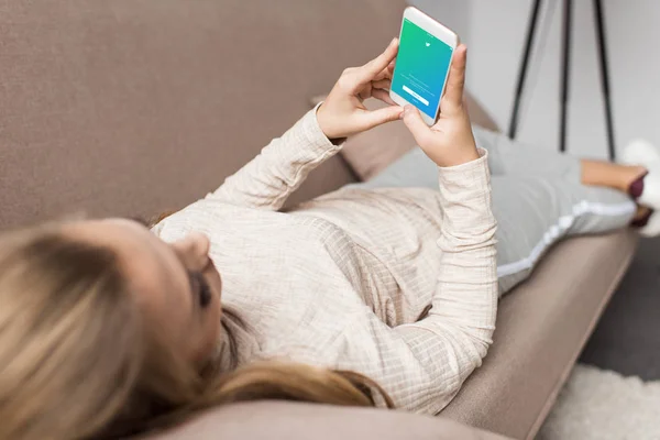 Mujer en el sofá utilizando el teléfono inteligente con la aplicación de twitter en la pantalla - foto de stock