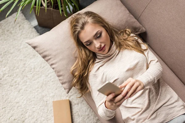 Blick aus der Vogelperspektive auf junge Frau, die ihr Smartphone auf der heimischen Couch benutzt — Stockfoto