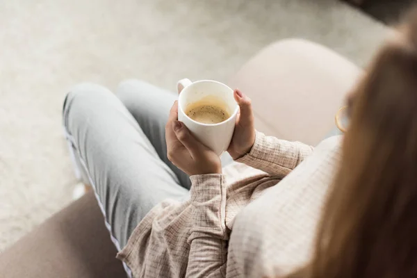 Cropped shot of woman with cup of coffee sitting on couch — Stock Photo