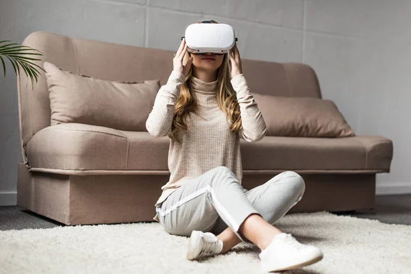 Mujer joven sentada en el suelo con auriculares de realidad virtual en casa - foto de stock